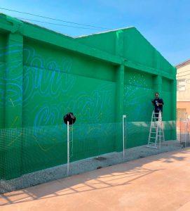 Concello e Migrarte colaboraron para esta estancia do artista Tomiño, 18 de setembro de 2024.- Tomiño mantén a súa firme aposta pola arte. O Concello acolle estes días por primeira vez ao artista internacional Marion Ve, un muralista colombiano recoñecido polas súas vibrantes creacións caligráficas que chegou ao municipio para deixar a súa pegada nun mural cheo de cor, enerxía e mensaxes inspiradoras na Avenida de República Arxentina. O antigo edificio do Palomar, xa na confluencia coa Praza do Seixo, será o lenzo da nova obra deste muralista que está de tour artístico por España realizando intercambios culturais que o levará a Valencia ou Barcelona e que decidiu recalar en Tomiño guiado da man da agrupación Migrarte. “Paréceme un sitio máxico, con espazos moi fermosos, por iso para min é moi emocionante pintar aquí e compartir a miña arte con toda a veciñanza”, explica. Unha interacción que poderá manterse ao longo desta semana, na que Marion Ve estará realizando o seu mural aberto ás preguntas e á charla cos veciños e veciñas, que poderán achegarse ao proceso creativo dun artista cunha traxectoria internacional que xa deixou a súa impronta en países como México ou Alemana. A súa obras, que levará o lema en galego ‘Sorrí, comparte a túa mellor enerxía’, é unha mostra do seu estilo único, que mestura ilustración, caligrafía e lettering. O seu obxectivo “é transmitir boa enerxía, facer que a xente sorría. Para min sorrir non é só a expresión da boca, é conectar cunha idea ou cun recordo que nos faga feliz. Cada persoa ten unha razón diferente para sorrir, só quero axudar a que cada quen atope a súa”, explica o autor. A alcaldesa de Tomiño, Sandra González, destaca a importancia desta colaboración co artista colombiano a través da plataforma Migrarte. “Para nós é un orgullo contar coa estancia de Marion Ve na nosa vila, un artista que co seu mural non só embelecerá as nosas rúas, senón que dará luz, cor e unha nova vida a unha medianeira. Tomiño é terra de artistas, e seguiremos apostando pola arte, tamén urbana, traballando para converter Tomiño nun espazo onde a cultura e a creatividade se respiren a cada paso”, salientou a rexedora. A plataforma Migrarte, que facilitou a chegada do artista a Tomiño, destaca a importancia destes intercambios para achegar a arte a novos espazos, diversificando circuítos e levando arte e artistas máis alá das grandes cidades. Agustina Patiño, representante da entidade, anima “a todos e todas as artistas e a todas as institucións e entidades a sumarse a estas iniciativas que enriquecen tanto ás e aos autores como ás comunidades que os acollen”. Novos murais Esta nova intervención en Tomiño únese a outros proxectos de arte mural que o Concello leva impulsando nos últimos meses. O máis recente é o mural realizado pola artista guardesa Tamara Baz na rúa de Gondomar, que homenaxea ao viveirismo, á planta e á muller, tan impoortantes no devir tomiñeses. Por outra banda, os muros do campo de fútbol de Goián é o lenzo dunha peza significativa do deporte e de Tomiño, facendo fincapé nos valores que transmiten como a igualdade e cunha referencia ao Goián FC, que realiza a súa actividade nestas instalacións. O mural forma parte do proxecto de mellora destas instalacións tamén a nivel estético, decorando medianeiras e espazos públicos, levando a arte aos veciños e visitantes e facendo de Tomiño un referente cultural. 